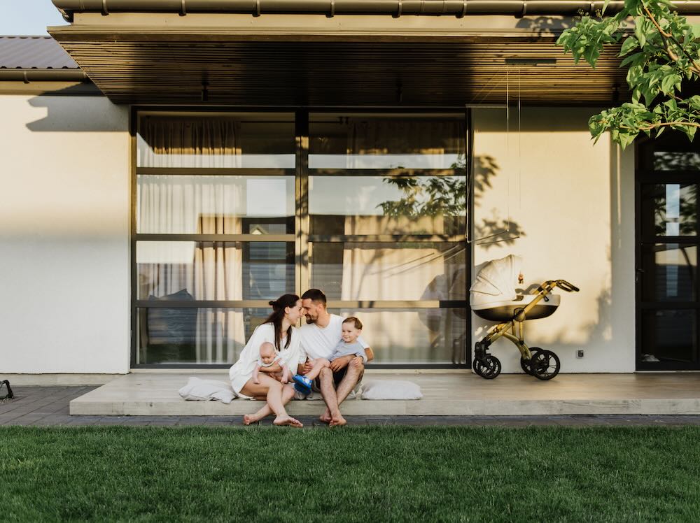 A young family with two little sons hug and kiss in the yard of their own house
