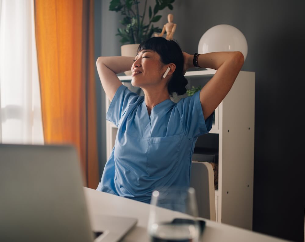 Female doctor resting in her office, eyes closed with headphones on 