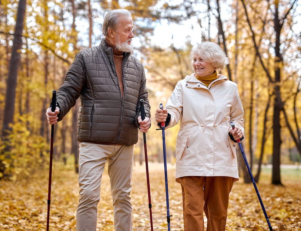 Senior caucasian european couple in casual wear walking with nordic walking poles in autumn park